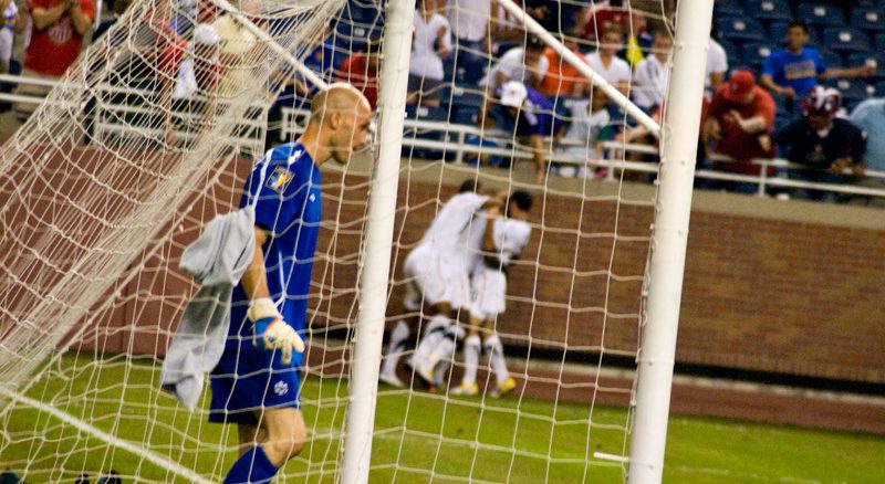 Canadian goalkeeper Lars Hirchfeld gathers his thoughts after giving up a bad first goal. The US players celebrate in the background.