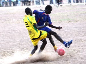 A Goozaga football team player (in yellow) challenging a Young Star player (in Blue) at Rumbek Stadium [©Gurtong]