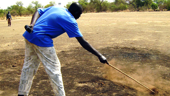 Mapel police officer, Mayen Atem pointing at the smoky substance and the burnt soil in Mapel [©Gurtong/ James Deng]