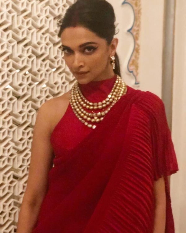 Deepika Padukone – her unmistakable elegance and ethereal charm is always a delight! She infuses life in ethnic ensembles and western ones with her lithe and svelte frame in tow and that hard-to-miss dimpled smile. The pre-wedding festivities, sangeet ceremony of Isha Ambani and Anand Piramal saw the new bride Deepika Padukone stun in a red ensemble from Faabiiana. Styled by Shaleena Nathani, Deepika pulled off the red ensemble from designers Kusum & Karishma Luharuwala’s label. Also Read: Sun, Sand and Bikini – Summer has officially begun for Deepika Padukone (View Pictures) The neo-Indian saree featured a pleated long train drape teamed with a halter neck backless blouse. Deepika upped the look with a layered necklace, earrings and her traditional red wedding chura. Also Read: INSIDE VIDEOS: Newlyweds Deepika Padukone – Ranveer Singh get groovy with Aishwarya Rai Bachchan, Sidharth Malhotra, Karisma Kapoor at Isha Ambani – Anand Parimal bash With sindoor in her forehead, Deepika sported a messy low back ponytail, courtesy hairstylist Gabriel Georgiou. Her glowy makeup featured winged defined eyebrows, nude lips and lightly contoured cheekbones, courtesy makeup artist Priya Todarwal. Also Read: Deepika Padukone BEATS Priyanka Chopra to be the SEXIEST woman in Asia On the professional front, Deepika Padukone was last seen as Rani Padmavati in Sanjay Leela Bhansali’s Padmaavat.