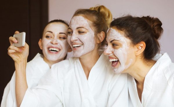 Three girl friends having a spa day and taking a selfie with face masks on